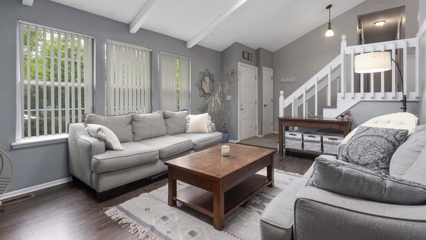 A living room with a gray sofa, a wooden coffee table, and a staircase with a white railing. - Family Favorite_Sleeps 8_Roomy_Game Room (Lenexa)