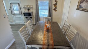 A dining room with a wooden table, white chairs, a ceiling fan, and a view of a backyard.