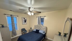A bedroom with a bed, a chair, a desk, a ceiling fan, and a window with curtains.
