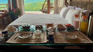 Uma mesa posta para o café da manhã, com pratos, tigelas e vista para uma paisagem montanhosa.