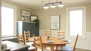 A dining area with a round table, six chairs, and a kitchen area with a cabinet and a window. - Coastal Farmhouse near Basin Head and Red Point (Lot 46)