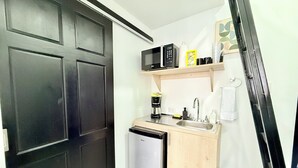 Eine kompakte Küche mit Kühlschrank, Mikrowelle, Kaffeemaschine und einer kleinen Spüle.