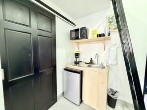 Cocina compacta equipada con refrigerador, microondas, cafetera y un lavamanos pequeño.
