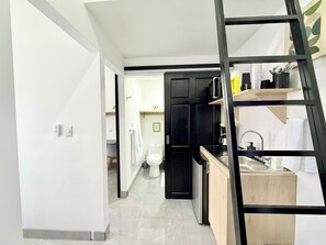 Una cocina moderna con una paleta de colores blanco y negro, encimera de madera y una escalera negra.