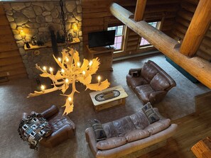 A log cabin interior with a stone fireplace, a wooden chandelier, leather sofas, and a television. - Charming 6-bedroom log cabin in Black Forest perfect for big groups (Colorado Springs)