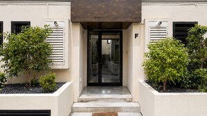 A modern building entrance with a glass door, a small outdoor seating area, and two planters with shrubs. - Bright and Elegant Apartment in La Marsa (La Marsa)