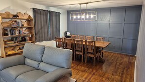 A living room with a sofa, wooden bookshelves, a dining table with chairs, and a modern pendant light. - The Bunk House at Kerr Lake (Henderson)
