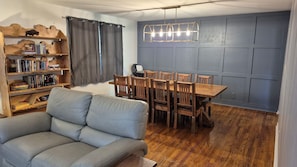 Un salon comprenant un canapé, des étagères en bois, une table à manger avec des chaises et un luminaire suspendu moderne.