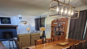 A dining area with a wooden table and chairs, a fireplace, and a bookshelf. - The Bunk House at Kerr Lake (Henderson)