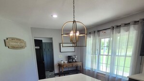 A spacious kitchen with a large island, wooden flooring, a hanging light fixture, and a view of the outdoors through large windows. - The Bunk House at Kerr Lake (Henderson)