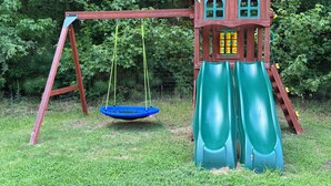 A wooden swing set with a slide, surrounded by greenery. - The Bunk House at Kerr Lake (Henderson)