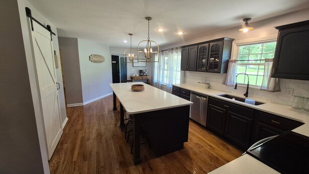 A kitchen with a central island, dark cabinets, and a window with curtains. - The Bunk House at Kerr Lake (Henderson)