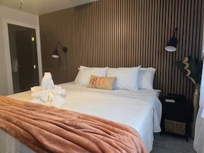 Et moderne hotelværelse med en seng, et natbord, en lampe og en væg med lodrette trælameller.