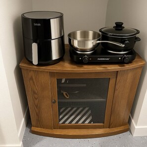 A kitchen with a black electric kettle, a stainless steel pot, and a black Farberware slow cooker on a wooden cabinet.