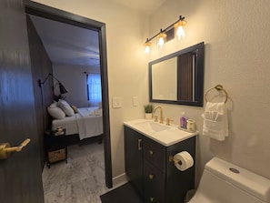 Et badeværelse med toilet, håndvask, spejl og håndklædestang.