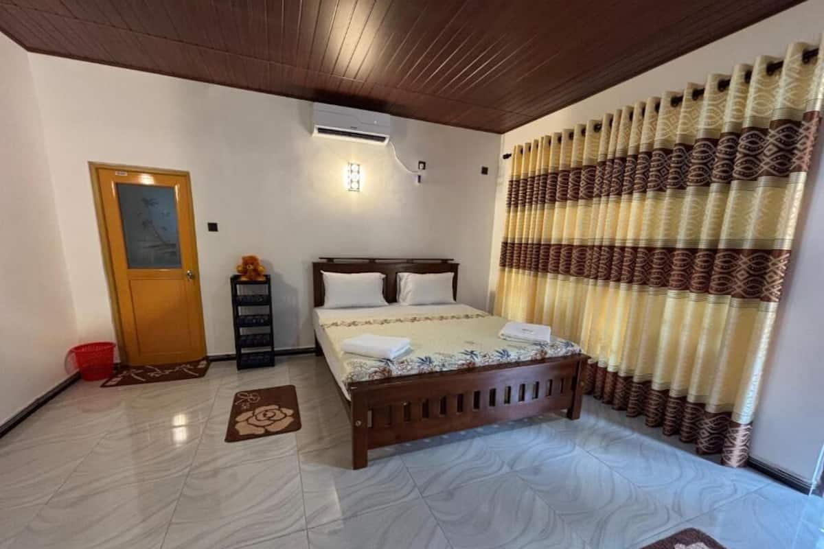 A bedroom with a wooden bed, a nightstand, a red basket, a door, and a patterned curtain.