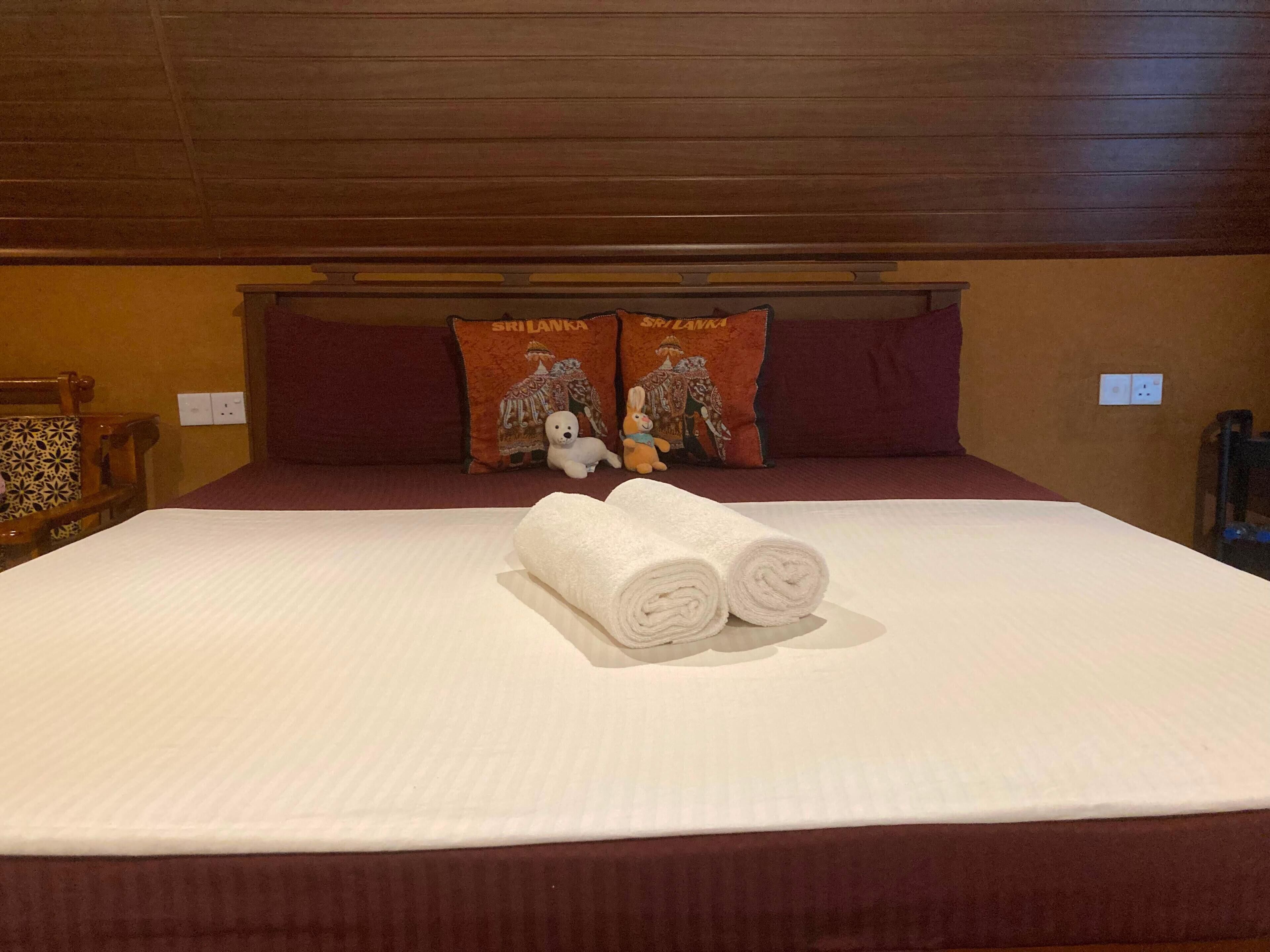 A hotel room with a bed, pillows, a chair, and a wall socket.