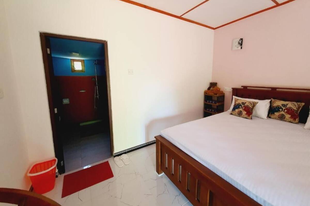 A bedroom with a bed, a red mat, a wooden headboard, a small shelf, and a door leading to another room.