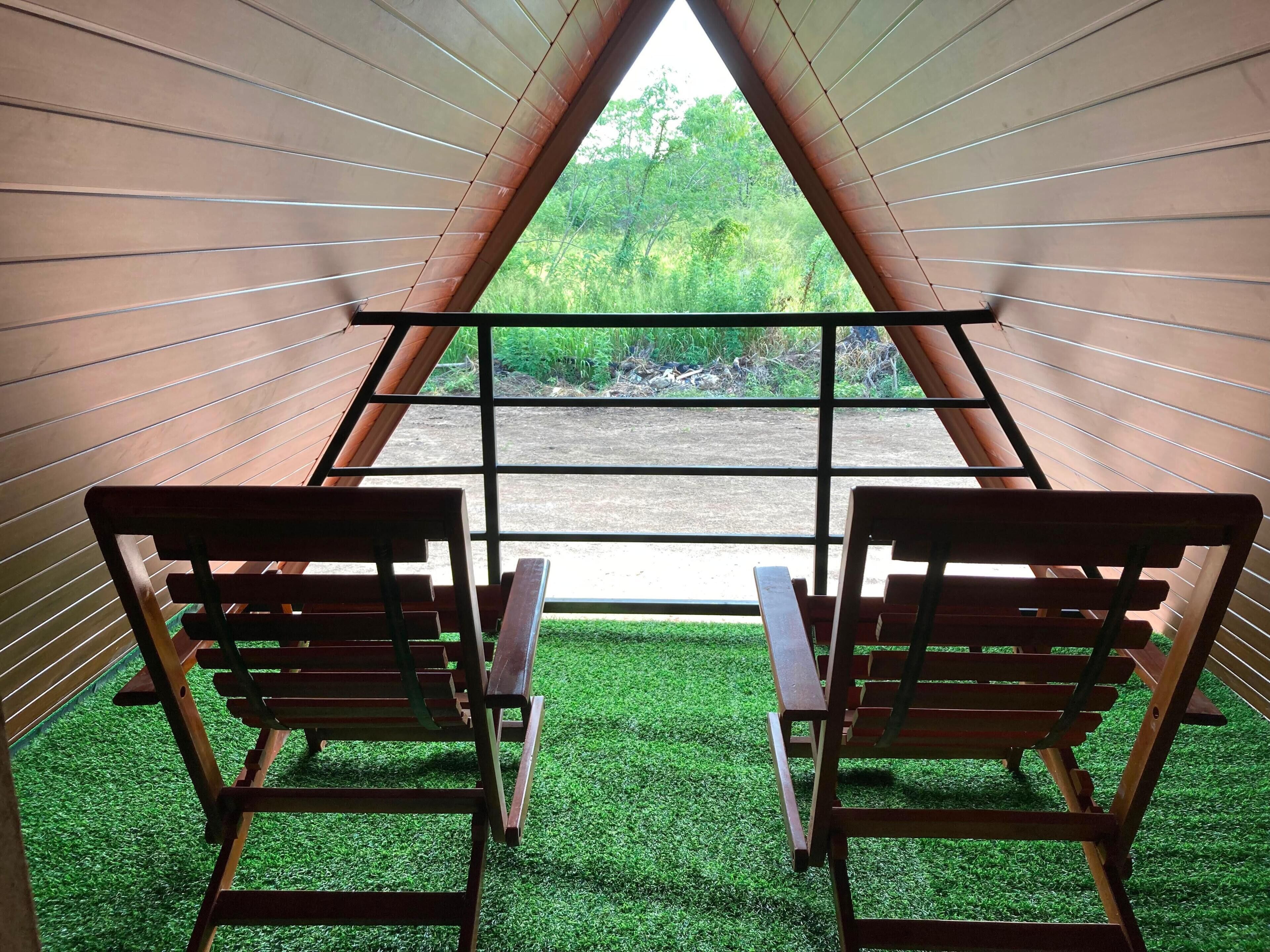 A room with two wooden chairs facing a window with a view of greenery.