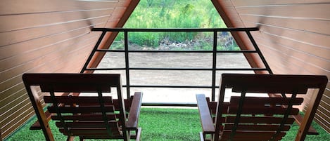 A room with two wooden chairs facing a window with a view of greenery.
