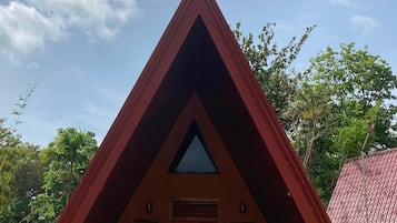 Een gebouw met een puntige dak, een centrale ingang en plantenbakken aan de voet, met een rode dakbedekking op de achtergrond.