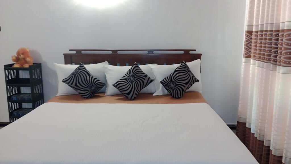 A bed with a wooden headboard, white bedding, and three black-and-white patterned pillows.