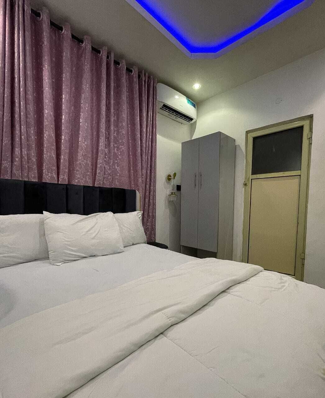 A bedroom with a bed, curtains, an air conditioning unit, a wardrobe, and a door.