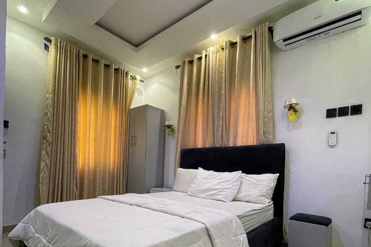 Hotellihuone, jossa on sänky, verhot, ilmastointilaite ja pieni roskakori.