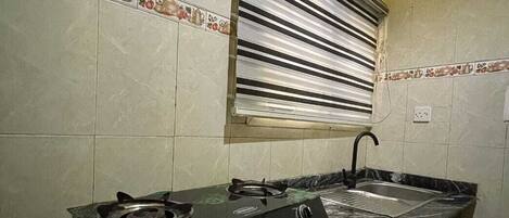 A kitchen with a gas stove, a sink, and a window with blinds.
