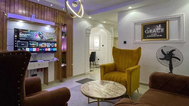 Una sala de estar moderna con una televisión de pantalla plana, una mesa redonda de centro, un sofá y una silla.
