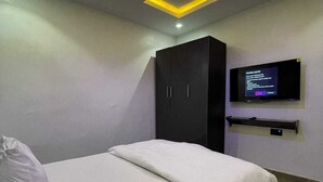Una habitación de hotel moderna con una cama, un armario, un televisor de pantalla plana e iluminación geométrica en el techo.