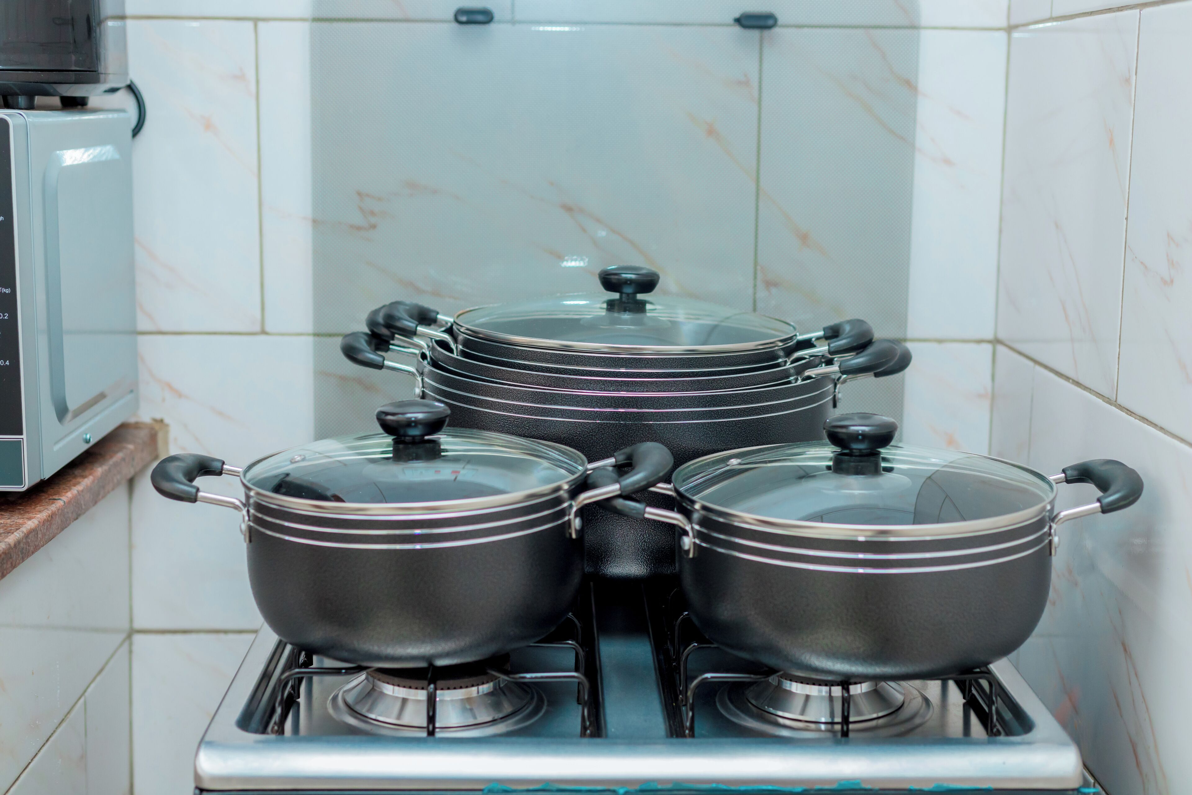 A kitchen with four pots on a stove, a microwave, and a tiled backsplash.