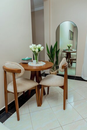 A dining area with two chairs, a table, a vase with flowers, a tissue box, and a mirror reflecting the room. - Modern Cozy Apartment, Fast WiFi & Balcony Views (Kampala)