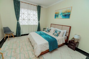 Quarto com cama, cadeira, mesa de cabeceira, quadro e janela com cortinas.