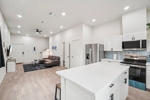 Eine moderne Küche mit weißen Schränken, einer großen Kochinsel, Edelstahlgeräten und einem Deckenventilator.