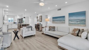A modern living room with a sofa, armchair, and a dining area with a table and chairs. - Runaway Bay 276 by Duncan Real Estate (Bradenton Beach)