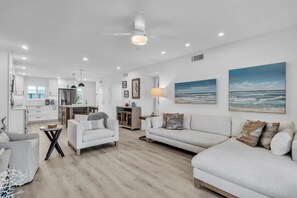A modern living room with a sofa, armchair, and a dining area with a table and chairs. - Runaway Bay 276 by Duncan Real Estate (Bradenton Beach)