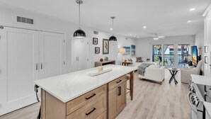 A modern kitchen with a marble countertop, wooden cabinets, pendant lighting, and a view of the outdoor balcony. - Runaway Bay 276 by Duncan Real Estate (Bradenton Beach)