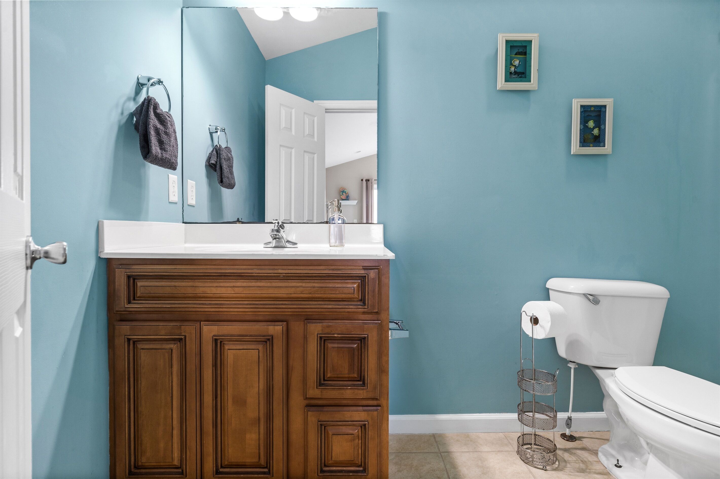 A bathroom with a wooden vanity, a white toilet, a mirror, and two framed pictures on the wall.