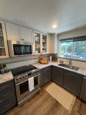 A modern kitchen with stainless steel appliances, a large window, and a view of the outdoors. - Private Resort • Pool, Spa + Sauna (Grants Pass)