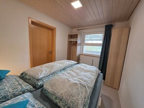 Une chambre avec deux lits, une porte en bois, une fenĂȘtre avec des rideaux et un radiateur.