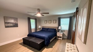A bedroom with a bed, bedside tables, a bench, a ceiling fan, and artwork on the walls. - Woodland Retreat/Pool+Patio+Firepit+SunsetViews (Weatherford)