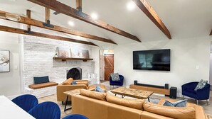 A spacious living room with a large sofa, blue chairs, a coffee table, a fireplace, and a TV mounted on the wall. - Woodland Retreat/Pool+Patio+Firepit+SunsetViews (Weatherford)