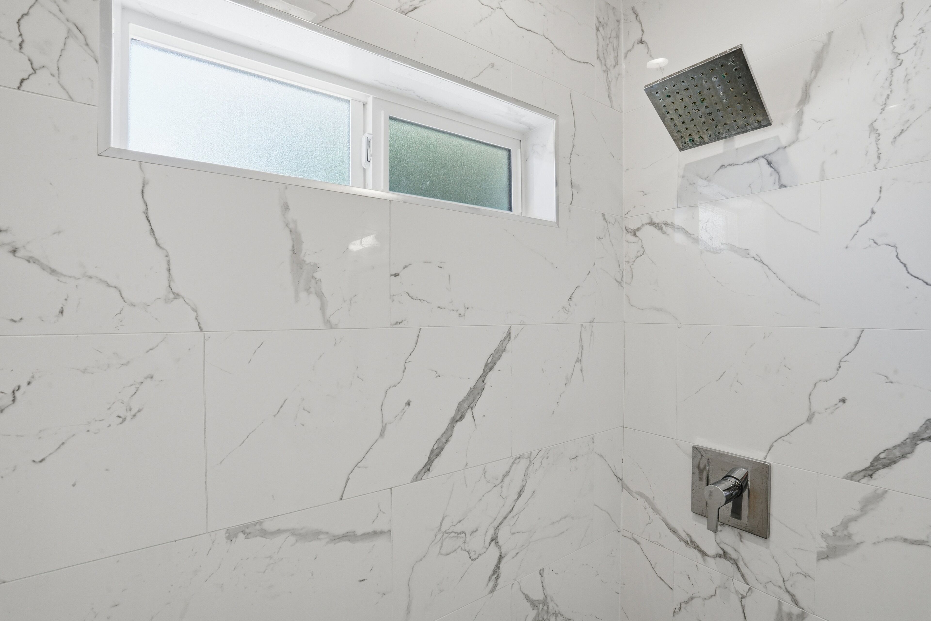 A bathroom with marble walls, a window, and a shower head.