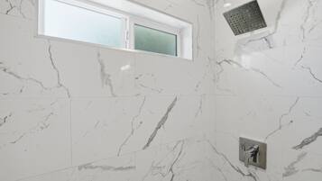 A bathroom with marble walls, a window, and a shower head.