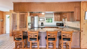 A kitchen with wooden cabinets, a stainless steel refrigerator, a microwave, and a bar area with stools. - Ultimate Lake Lure Vacation Home with Boat Dock (Lake Lure)