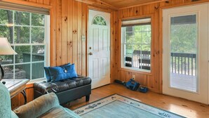 A wooden cabin interior with a leather couch, a rug, and a door leading to a deck. - Ultimate Lake Lure Vacation Home with Boat Dock (Lake Lure)
