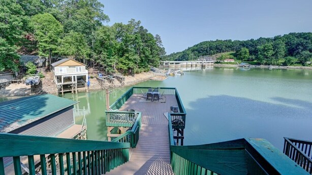 A riverside dock with a wooden deck, a small building, and a bridge in the background. - Ultimate Lake Lure Vacation Home with Boat Dock (Lake Lure)