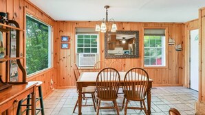 A wooden-paneled room with a dining table, chairs, a chandelier, and a large window. - Ultimate Lake Lure Vacation Home with Boat Dock (Lake Lure)