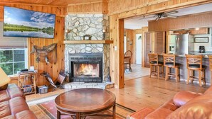 A cozy cabin interior with a stone fireplace, wooden walls, a television, and a dining area. - Ultimate Lake Lure Vacation Home with Boat Dock (Lake Lure)